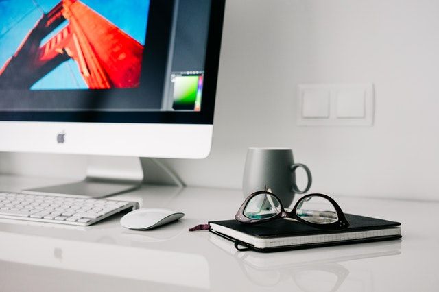 Mac auf weißem Schreibtisch mit Notizheft neben der Tastatur